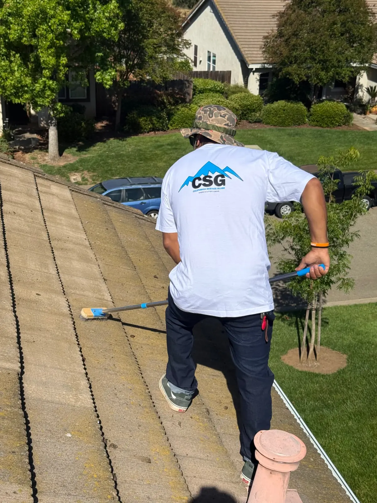 CSG technician brushing moss and debris from a concrete tile roof in Rancho Cordova, California