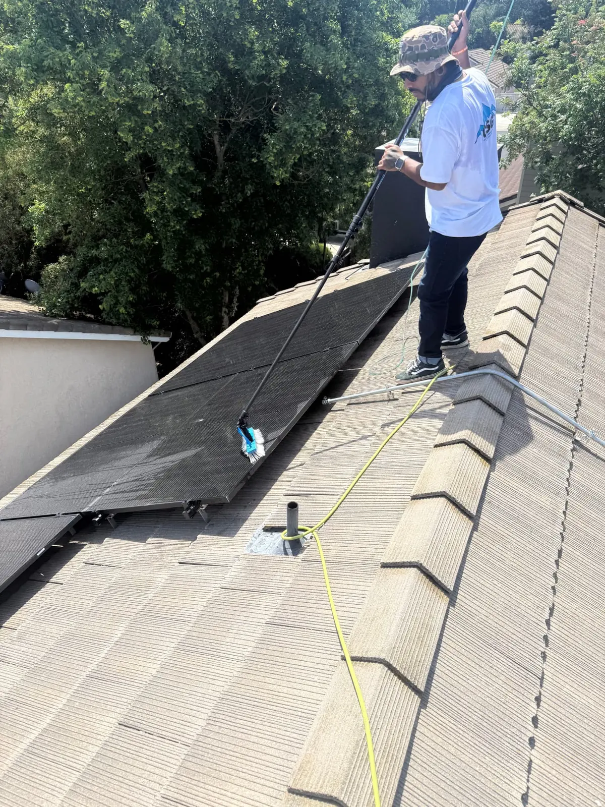 CSG technician brushing a rooftop solar array with a soft water-fed brush on a tile roof