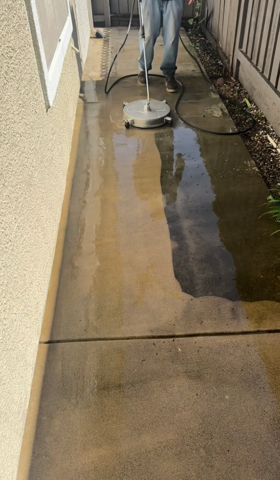 CSG technician cleaning a concrete side walkway with a rotary surface cleaner, showing the clean strip against the dirty concrete