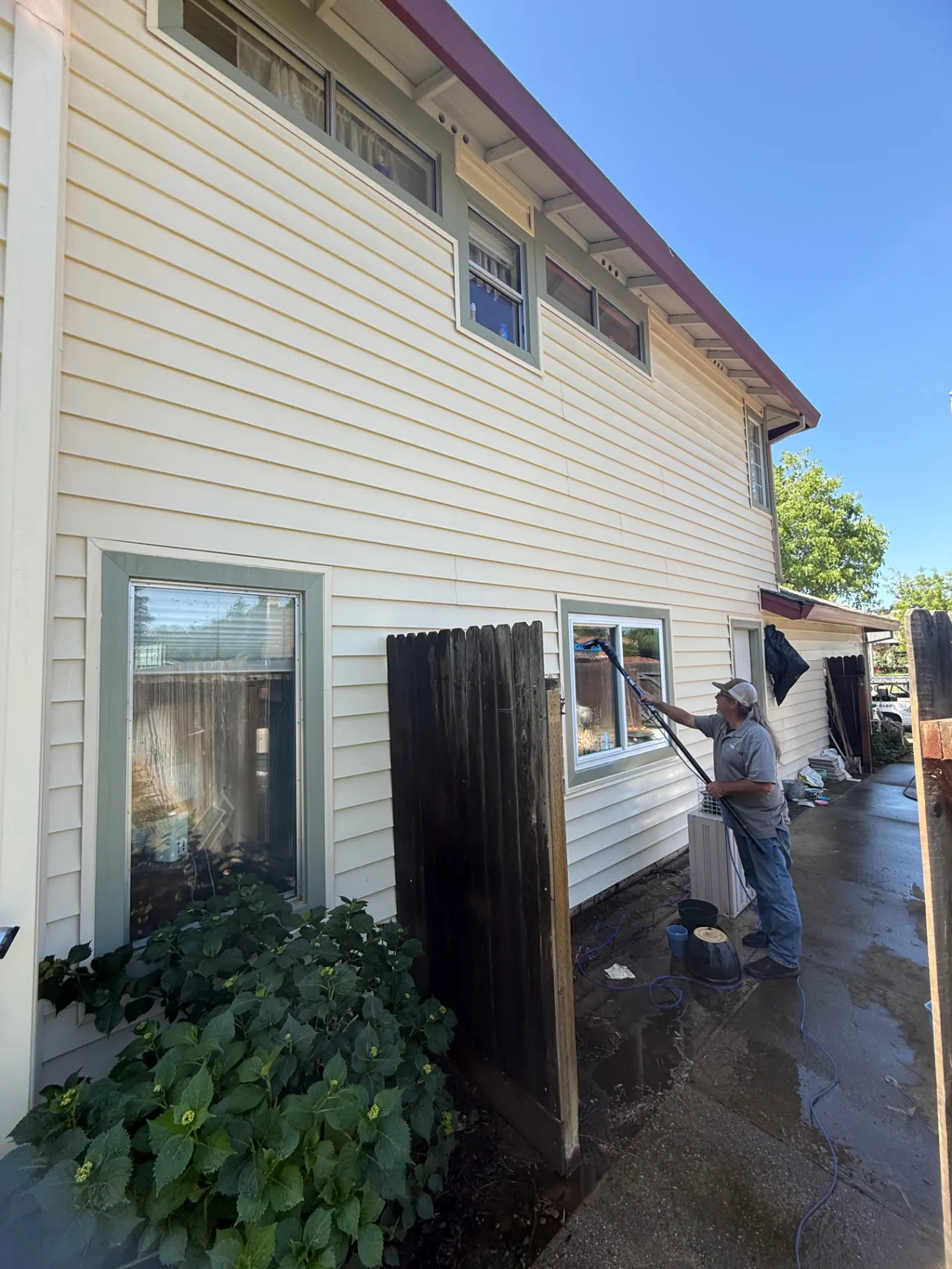 CSG technician working on the lap siding and windows of a two-story Sacramento home with a water-fed pole
