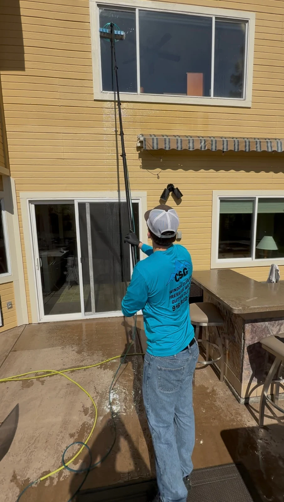 CSG technician cleaning second-story windows from the ground with a water-fed pole