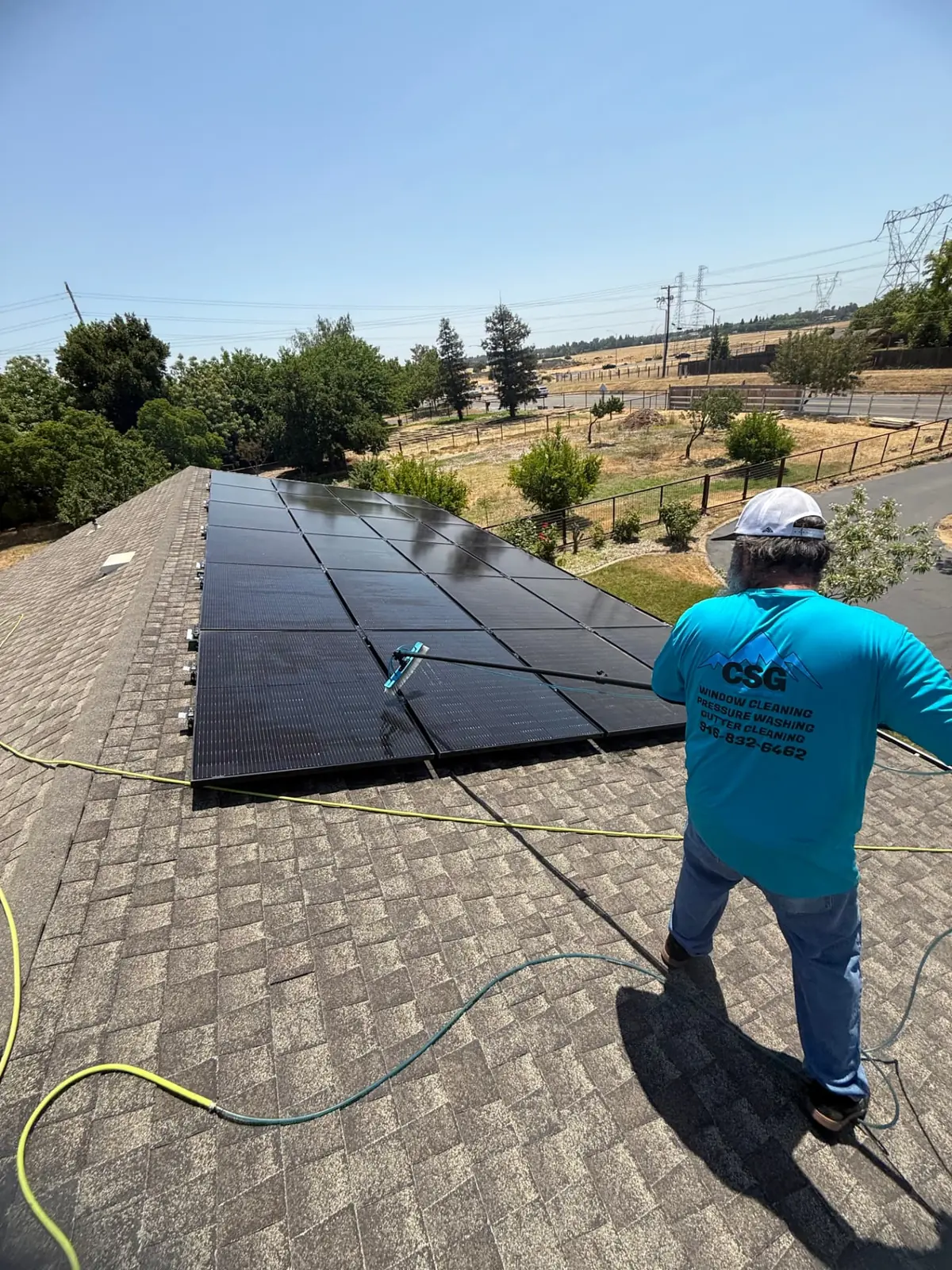 CSG technician washing a full rooftop solar array with a water-fed pole on an Elk Grove home