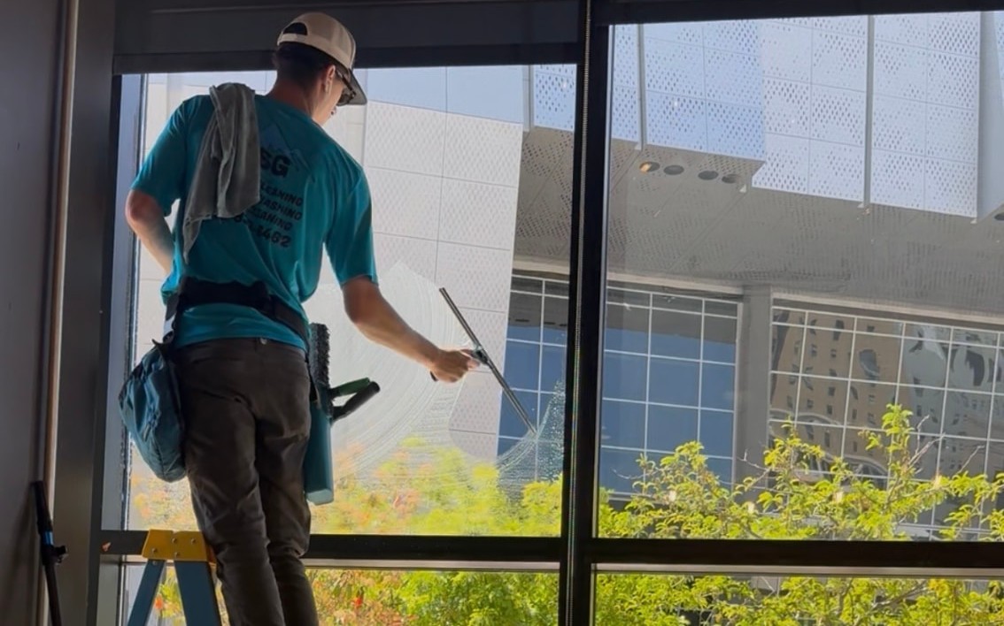 CSG technician on a ladder squeegeeing tall interior glass at a hair salon in downtown Sacramento