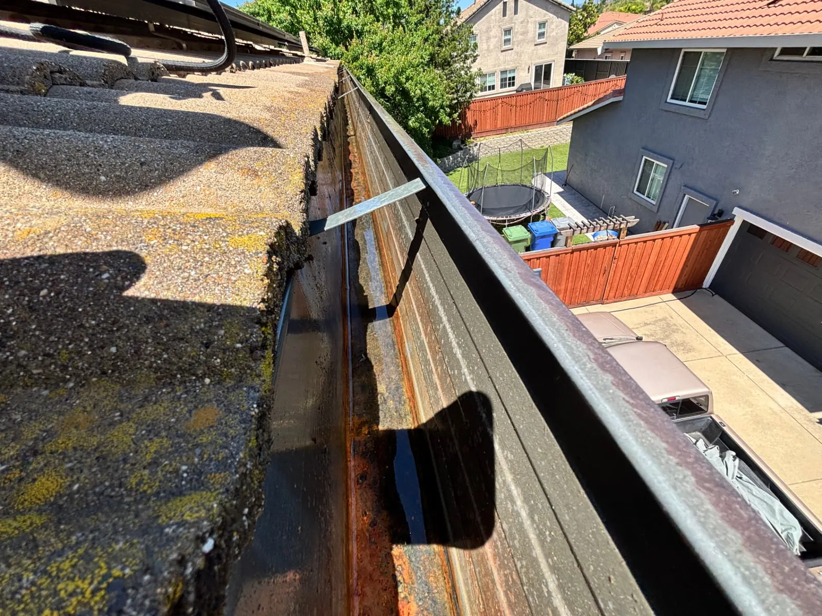 Rain gutter along a Folsom rooftop with packed grit and organic buildup being cleared during a CSG gutter cleaning
